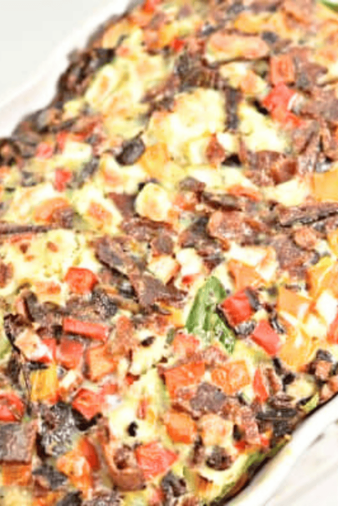 Freshly baked spinach and feta egg bake in a white dish, filled with colorful bell peppers, crispy bacon, and leafy greens—perfect for a savory keto breakfast or low carb egg bake recipe.