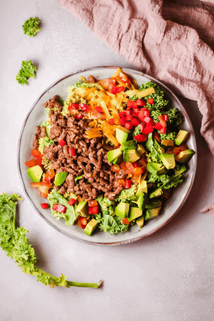 Overhead shot of a vibrant keto taco salad with fresh vegetables and cooked beef served on a ceramic plate.