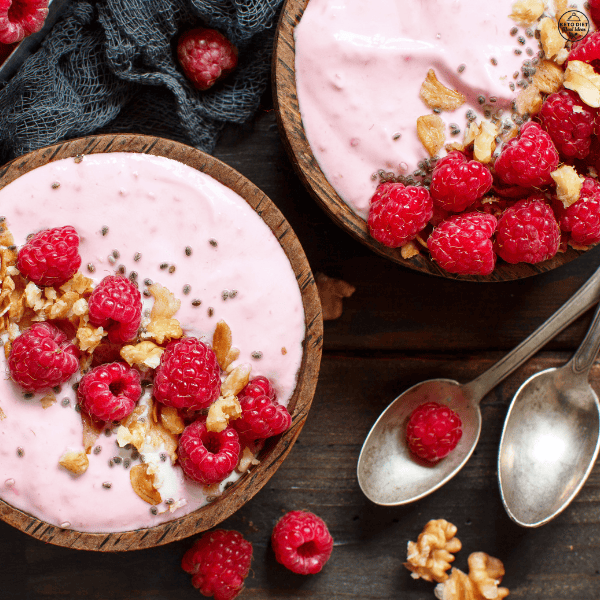 A creamy raspberry smoothie bowl topped with fresh raspberries, walnuts, chia seeds, and toasted coconut flakes, served in a wooden bowl.
