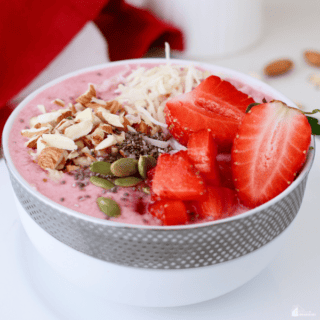 A keto smoothie bowl with a creamy pink base, topped with fresh strawberries, shredded coconut, chopped almonds, chia seeds, and pumpkin seeds in a stylish white bowl.