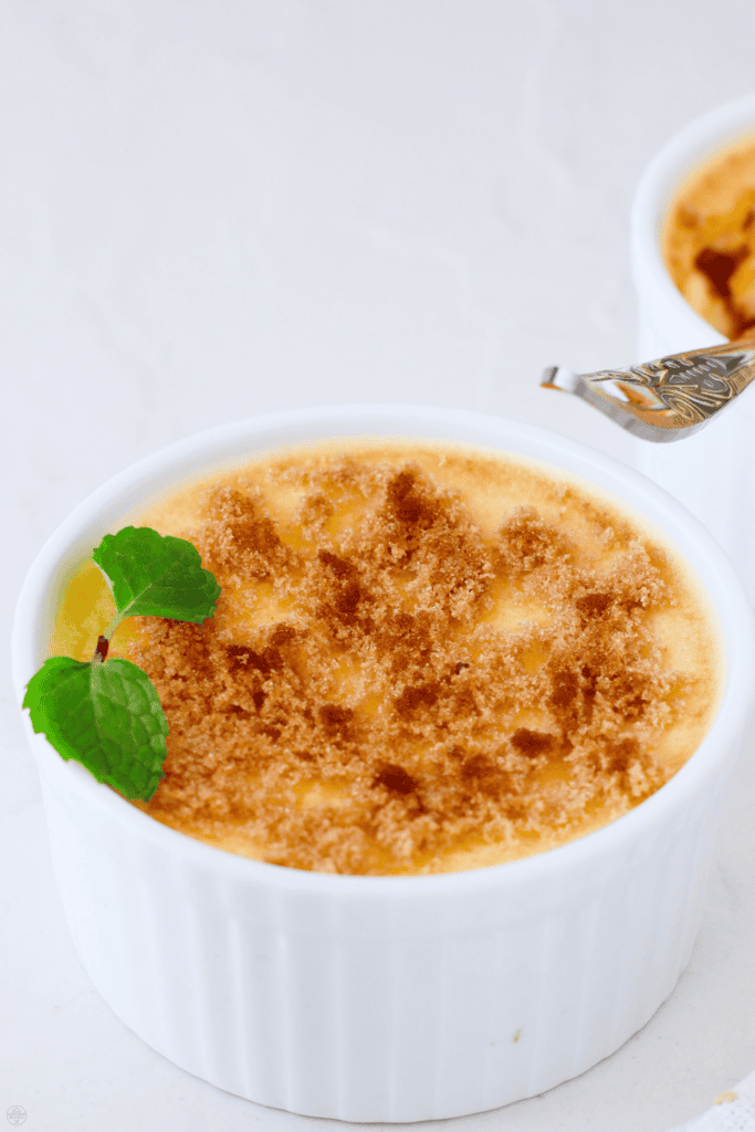 Close-up of keto creme brulee in a white ramekin topped with golden, sugar-free crust and a fresh mint garnish.