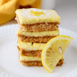 A tall stack of keto lemon bars with a golden almond flour crust and bright lemon filling, served with a fresh lemon wedge.
