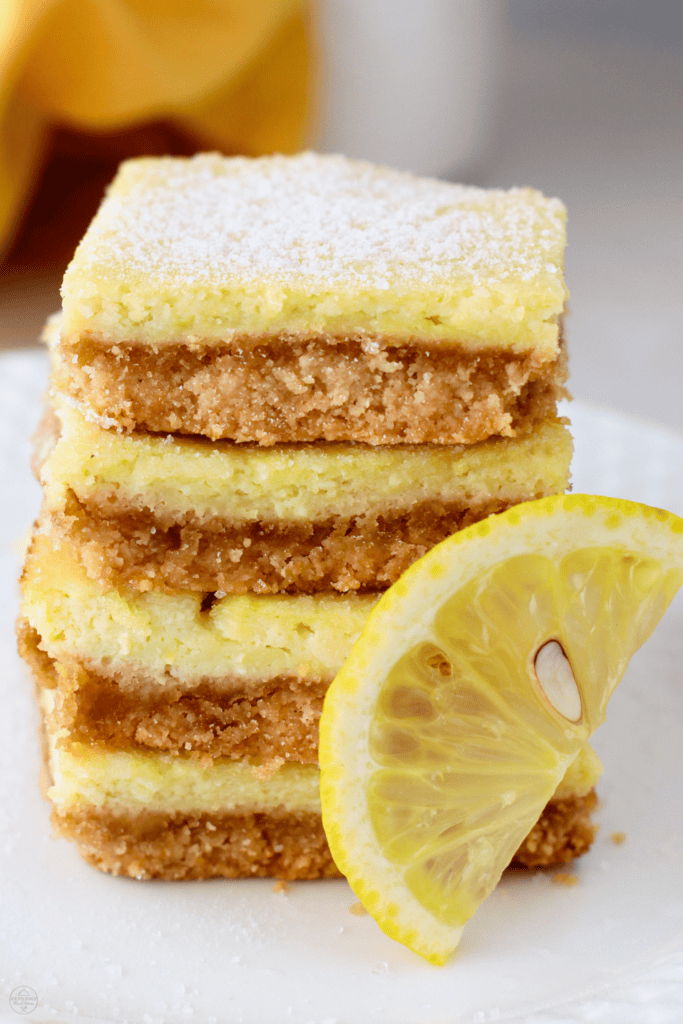 Close-up of gluten-free keto lemon bars stacked neatly, highlighting the thick crust and creamy lemon layer with a lemon wedge.