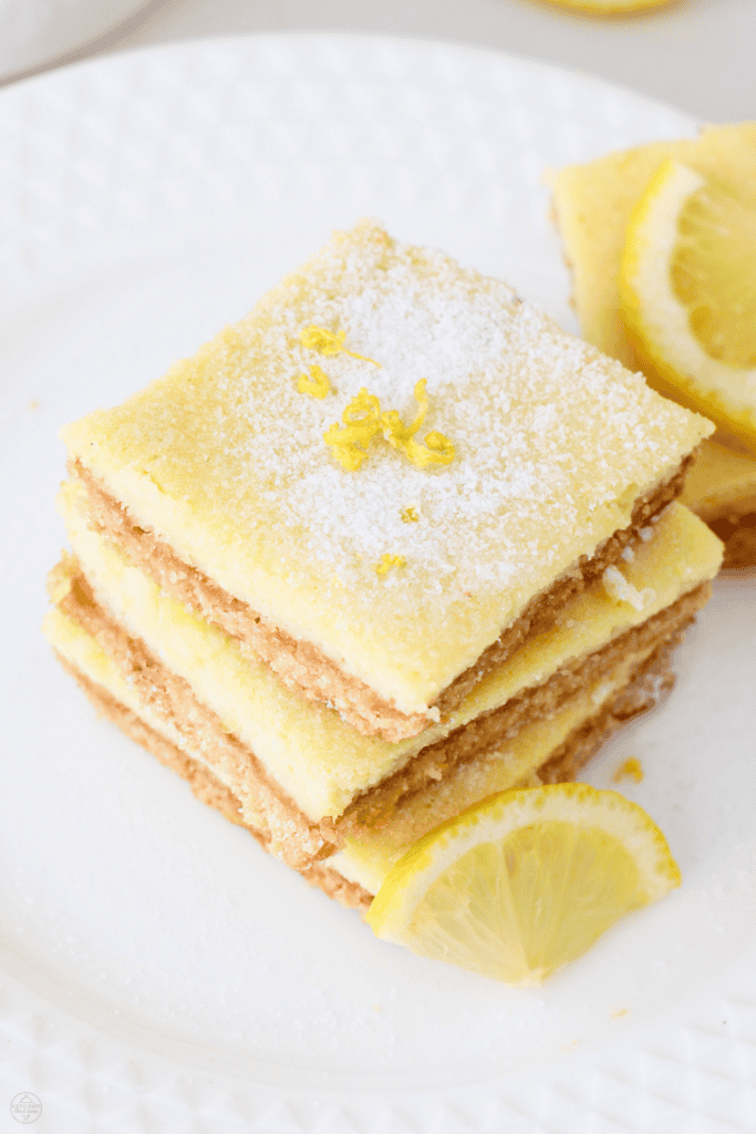 A plate of low carb lemon bars topped with lemon zest and paired with fresh lemon slices for a vibrant dessert presentation.