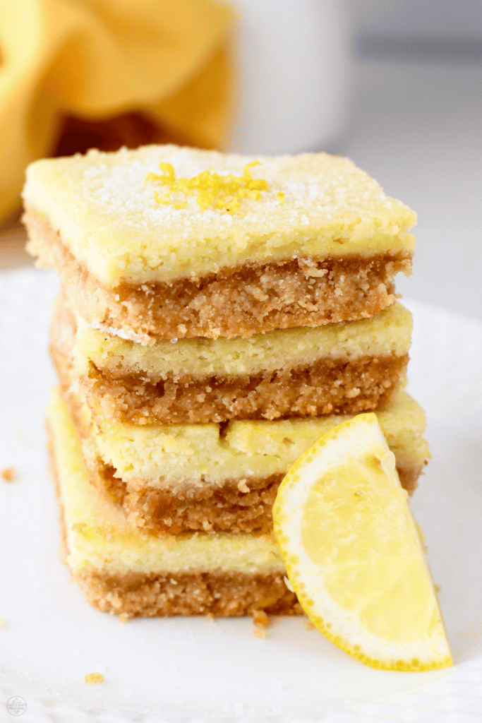 A tall stack of keto lemon bars with a golden almond flour crust and bright lemon filling, served with a fresh lemon wedge.