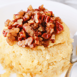 A single-serve keto pecan pie mug cake plated and topped with caramelized chopped pecans.