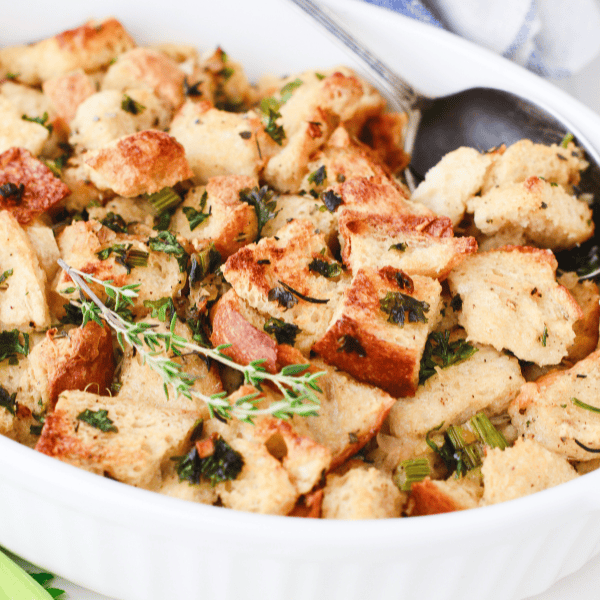 Close-up of golden, toasted low carb stuffing made with keto bread, herbs, and celery in a white baking dish.