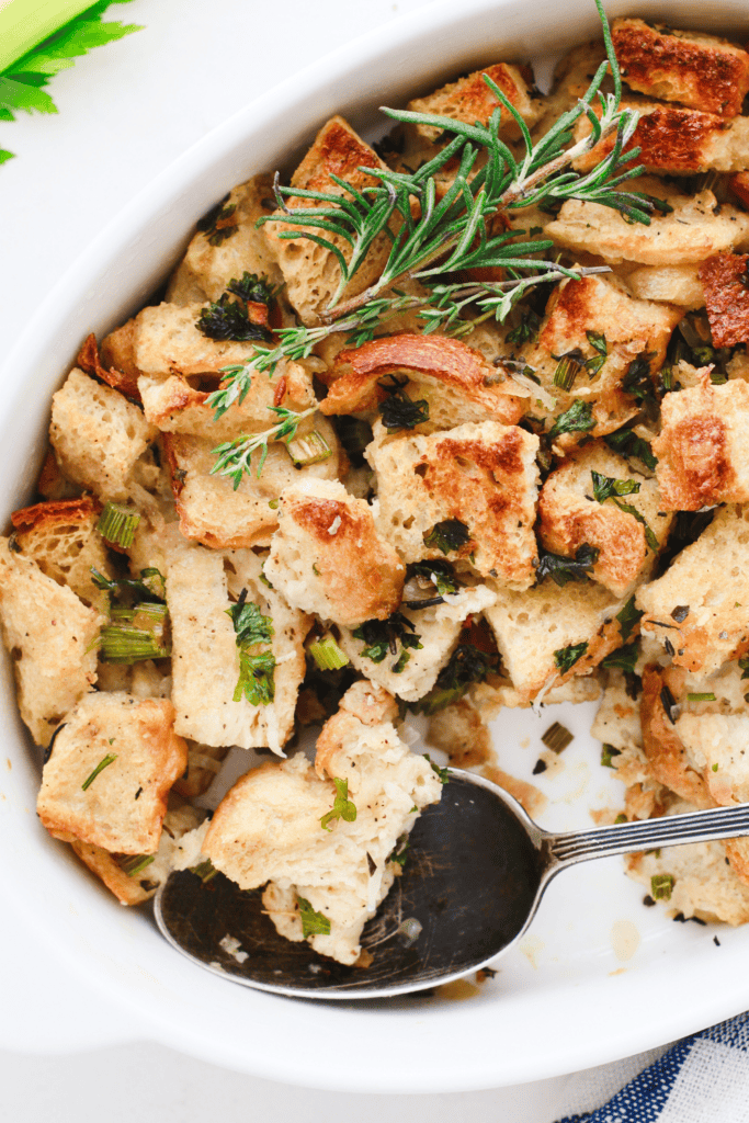 Overhead view of baked keto stuffing in a white dish, topped with fresh herbs like rosemary and thyme.