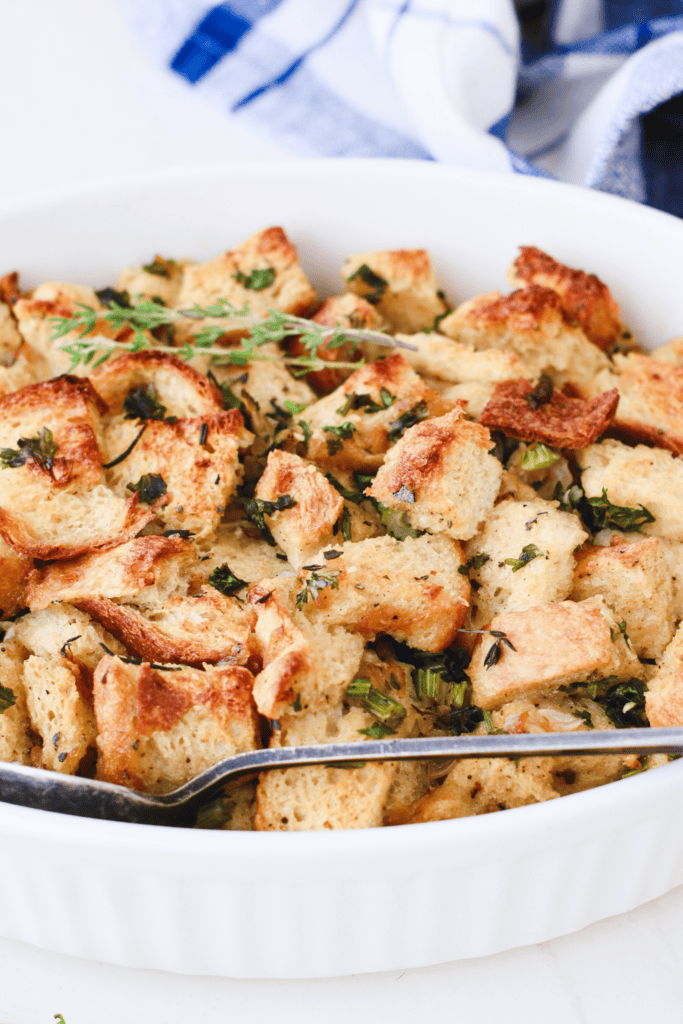Side angle of a white casserole dish filled with easy keto stuffing, showing crispy edges and vibrant herbs.