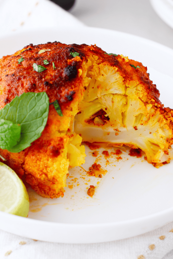 Side angle of crispy roasted tandoori cauliflower showing its texture, cut open and served with mint leaves and lime.