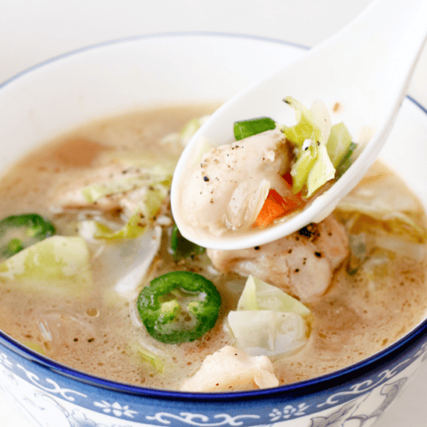Side view of a bowl filled with low carb cabbage soup garnished with jalapeños and green onions, with fresh herbs nearby.
