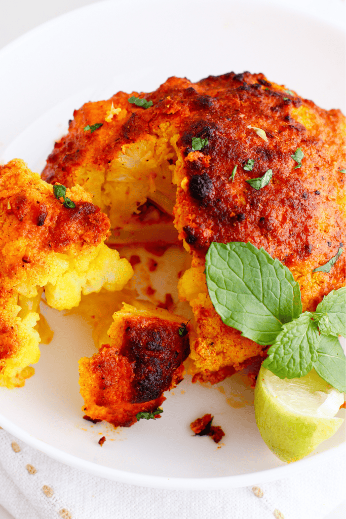 Close-up of roasted tandoori cauliflower sliced open to reveal the tender, golden interior, garnished with mint and lime.