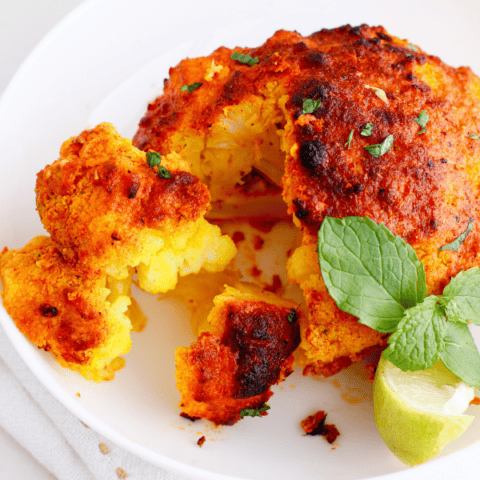 Close-up of roasted tandoori cauliflower sliced open to reveal the tender, golden interior, garnished with mint and lime.