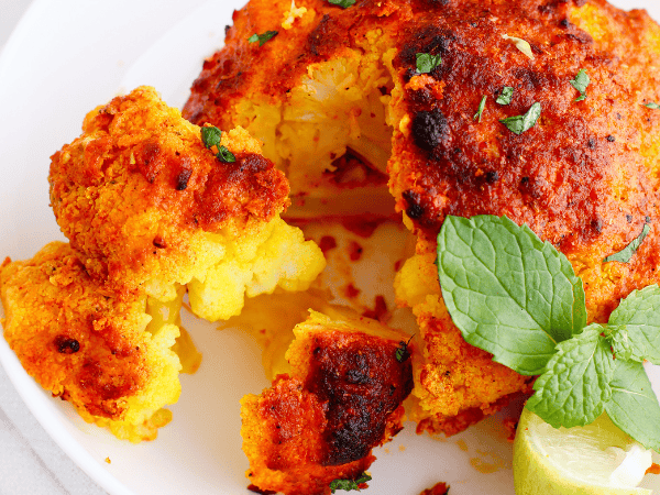 Close-up of roasted tandoori cauliflower sliced open to reveal the tender, golden interior, garnished with mint and lime.