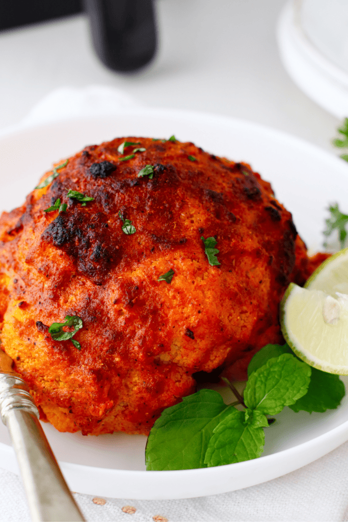 Roasted tandoori cauliflower served on a plate with a fork, fresh mint, and a lime wedge on the side.