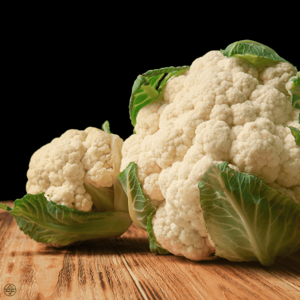 Two fresh cauliflower heads with green leaves on a wooden surface, considered as a good substitute for chickpeas.