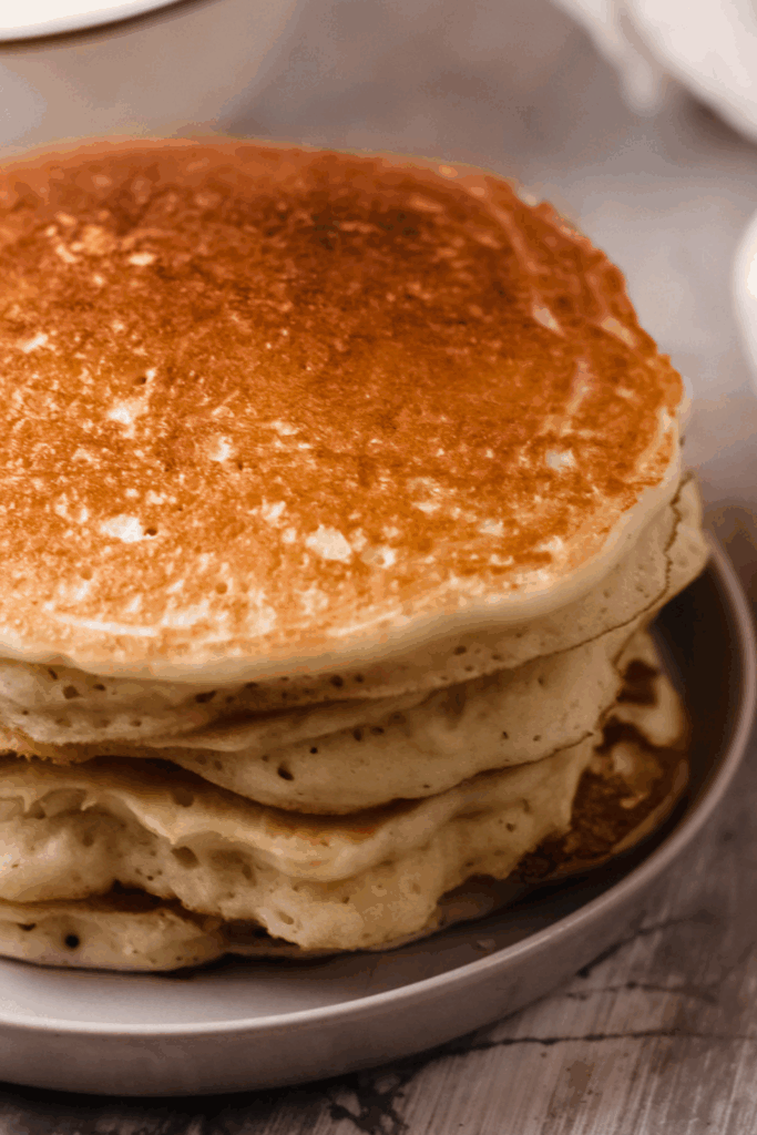 A close-up of a tall stack of golden-brown keto pancakes on a plate.