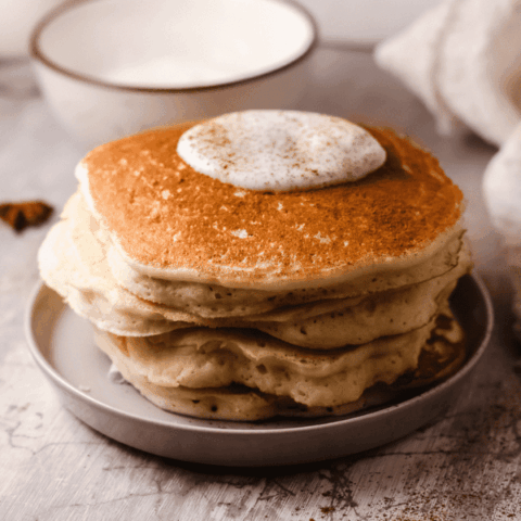 A close-up side view of fluffy keto pancakes topped with whipped cream and sprinkled with cinnamon.