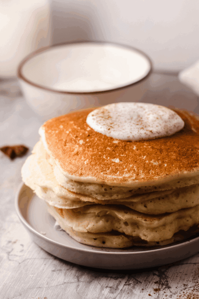 A close-up side view of fluffy keto pancakes topped with whipped cream and sprinkled with cinnamon.