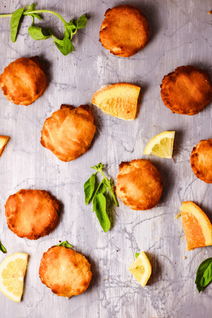 Keto citrus cheesecake cookies made with coconut flour and cream cheese arranged on a light surface with fresh lemon and orange slices, showing golden low carb cookies with a soft cheesecake texture.